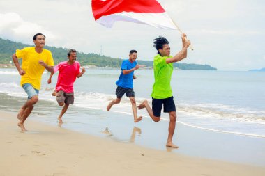 Bağımsızlık Günü 'nü kutlayan Endonezya bayrağıyla plajda koşan bir grup adam.