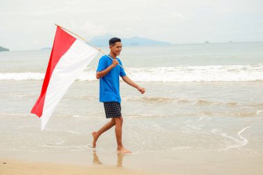 Genç adam ulusal bayrağıyla tropik bir plajda Endonezya Bağımsızlık Günü 'nü kutluyor.