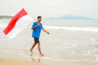 Genç bir adam sahilde yürürken Endonezya 'nın Bağımsızlık Günü' nü kutluyor..