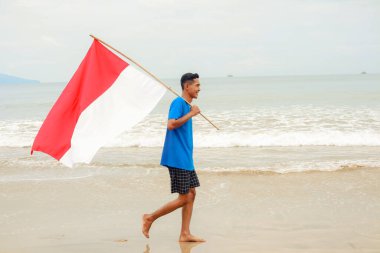 Genç bir adam Endonezya bayrağını taşıyarak sevinçle sahilde yürüyor özgürlüğünü kutluyor.