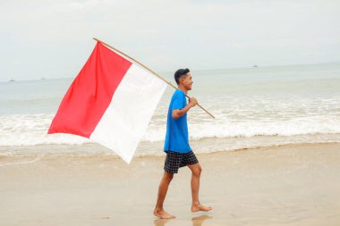 Genç adam gururla Endonezya bayrağını sahilde taşıyor, bağımsızlığını kutluyor.