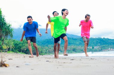Canlı tişörtler giymiş, Tropik bir plajda koşan dört genç adam.