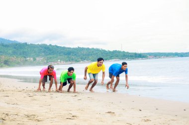 Genç adamlar Parlak Gökler Altında Sahil Yarışı için Hazırlanın Renkli Gömlekler ve Mavi Okyanus