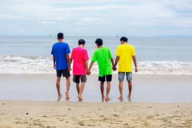 Dört Genç Adam Kumsalda Renkli Tişörtler Denizi 'nde El ele Yürümenin keyfini çıkarıyor