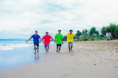 Canlı tişörtlü dört kişi Sandy Beach 'te koşuyor.