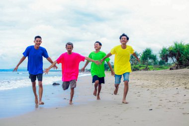 Renkli gömleklerle kumsalda neşeyle koşan dört kişi.