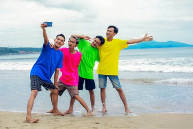 Mutlu insanlar güneşli bir sahilde selfie çekiyor.
