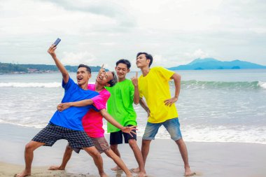 Bir grup arkadaş güneşli bir sahilde selfie çekiyorlar.