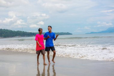 Okyanus kıyısındaki kumsalda yürüyen ve konuşan iki insan.