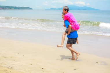 Mutlu son sınıf çifti, güneşli bir plajda sırtımda gezintiyle eğleniyor.