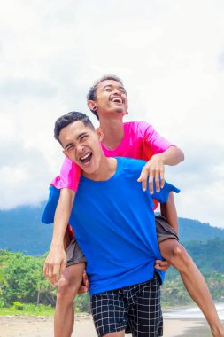 İki mutlu genç adam güneşli bir plajda sırtımda gezintiye çıkıyor.