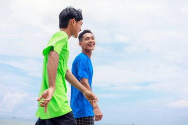 Güneşli bir sahilde yürüyen iki genç adam.