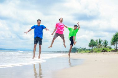 Güneşli bir sahilde zıplayan üç mutlu insan.