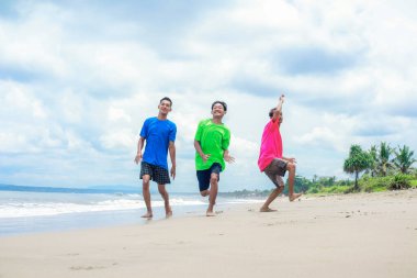 Tropik bir plajda neşeyle koşan üç genç adam