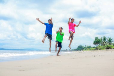 Güneşli bir sahilde neşeyle zıplayan üç genç adam.
