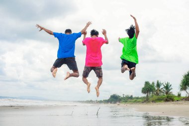 Tropik bir plajda neşeyle zıplayan üç kişi.