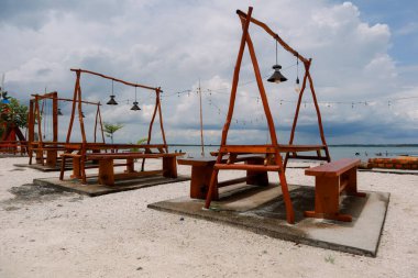 Kumsaldaki ahşap piknik masaları büyüleyici bir sahil manzarası yaratır.