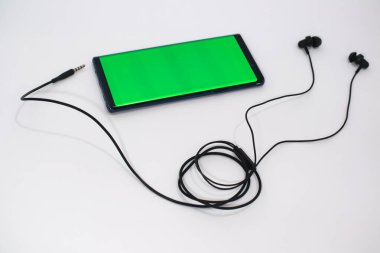Beyaz arka planda siyah kablo kulaklıklara bağlı yeşil ekranlı akıllı telefon.