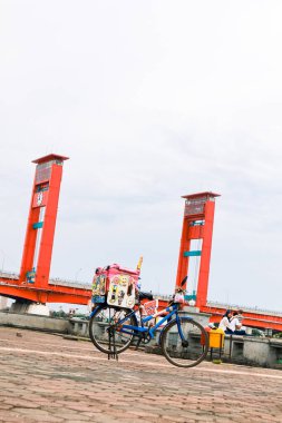 Parlak bir günde Ampera Köprüsü 'nün önüne park edilmiş şeker ve süslemeli mavi bisiklet.