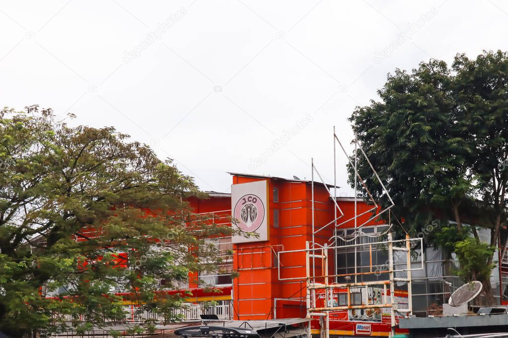 View of an orange building with a unique logo under an overcast sky surrounded by green trees.