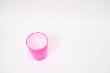 Düz beyaz bir yüzey üzerinde küçük, boş, canlı, pembe bir fincanın yakın görüntüsü. Bardak hafif kıvrımlı tabanlı silindirik ve görüntünün merkezinden biraz sapmış.