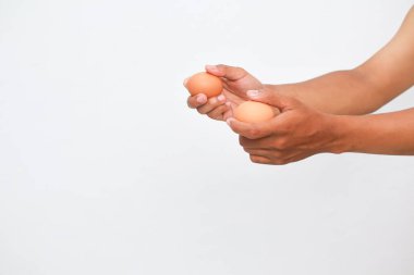 İki kahverengi yumurtanın, bir insanın ellerinde sade beyaz bir arka plana nazikçe tutunuşunu yakından izleyin. Görüntü, yumurta ve ellere odaklı olarak basitçe aydınlatılıyor.