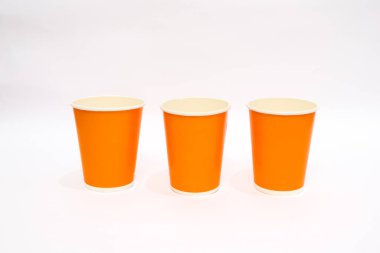 Üç turuncu kağıt bardak düz beyaz bir arkaplanda dururlar, temiz ve basit.