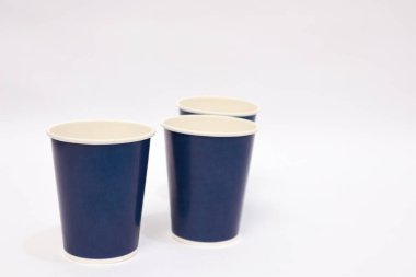 Temiz beyaz bir zemin üzerinde üç koyu mavi kağıt bardak minimalist kompozisyon, sergi tasarımı ve kamu hizmeti
