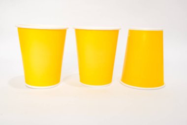 Beyaz arka planda üç sarı kağıt bardak, biri baş aşağı, içecek veya parti konsepti için minimum tasarım