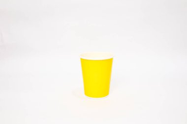 Canlı sarı bir kağıt bardak, içecekler ve minimalist tasarımlar için ideal beyaz bir zemin üzerinde oturur.