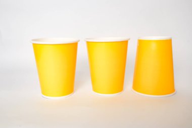 Üç parlak sarı bardak, temiz beyaz arka planda bir sırada duruyor..