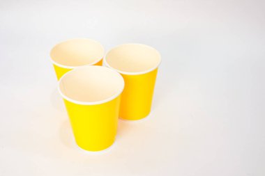 Üç tane parlak sarı kağıt bardak temiz beyaz bir zemin üzerine yerleştirilmiştir. Sürdürülebilir ve tek kullanımlık içecek malzemelerini göstermek için idealdir..