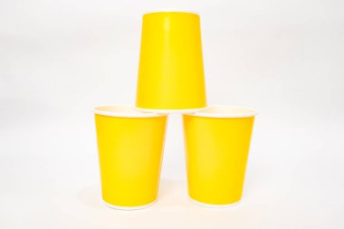 Temiz beyaz arka planda izole edilmiş üç parlak sarı kağıt bardaktan oluşan bir piramit. Basit ve canlı..