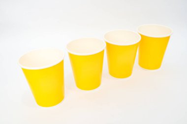 Parlak sarı kağıt bardaklar parlak ve minimalist bir görsel için temiz beyaz bir zemin üzerine dizilmiştir..