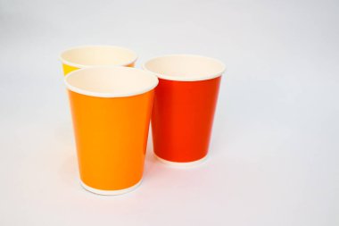 Üç renkli kağıt bardak, turuncu, kırmızı ve sarı, temiz, minimalist bir tasarım için beyaz arka planda sergileniyor.