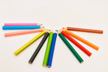 Fan şeklinde dizilmiş çeşitli renkli kalemler, temiz beyaz bir arkaplanda izole edilmiş.