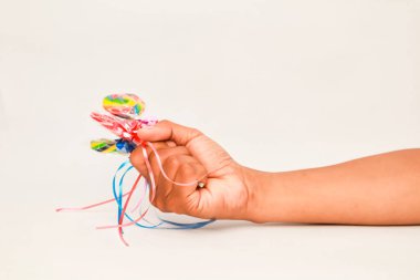 Beyaz arka planda kurdeleli renkli lolipoplar tutan bir el.