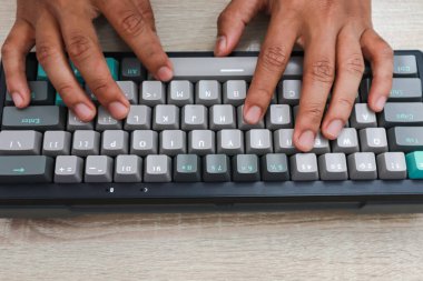 Açık ahşap bir yüzey üzerinde gri mekanik bir klavyeye yazı yazan elleri kapat