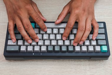 Açık ahşap bir yüzey üzerinde mavi ve gri bir klavyeye yazı yazan eller.