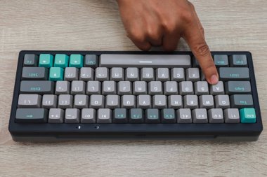 Tahta bir yüzey üzerinde bir kişinin elinin, gri ve gök mavisi mekanik bir klavyeye basarak yakınlaşması.