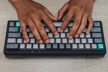 Tahta bir yüzey üzerinde mavi ve gri mekanik bir klavyeye yazı yazan elleri kapatın