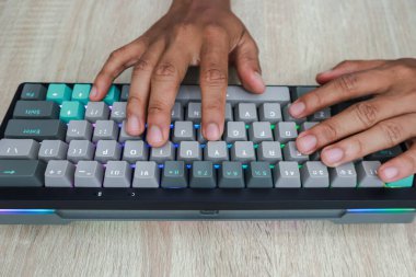 Açık bir ahşap üzerinde mavi, gri ve bej tuşlarla kişiselleştirilmiş bir klavyeye yazı yazan elleri kapatın