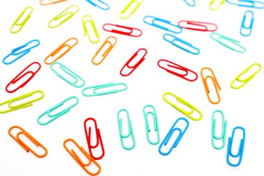 Beyaz arkaplana saçılmış çeşitli renkli ataçlar eğlenceli ve düzenli bir resim oluşturur