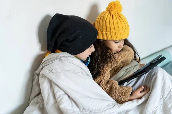 stock image Children sitting in a bed in home in cold winter time. Siblings together warms in blanket and using tablet.