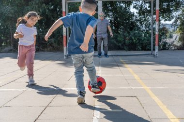 Mutlu aile futbol oynuyor. Futbol topunu tekmeleyen çocuğun arka görüntüsü. Küçük kız koşuyor. Büyükbaba futbol kalecisi kaleyi koruyor..