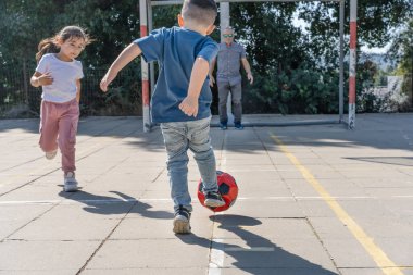 Mutlu aile futbol oynuyor. Futbol topunu tekmeleyen çocuğun arka görüntüsü. Küçük kız koşuyor. Büyükbaba futbol kalecisi kaleyi koruyor..