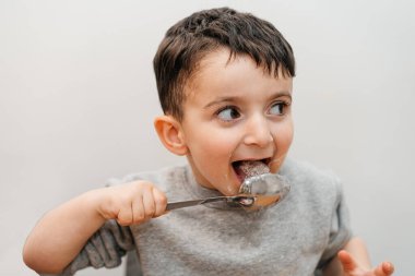 Funny child licks a spoon with sugar. Portrait joyful beautiful boy eating sugar and looking away.