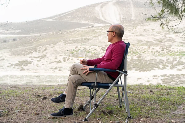 Man sitting on folding chair with glass of wine, admiring the beautiful views of nature.