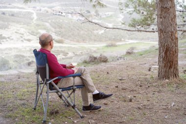 Man sitting on folding chair with glass of wine, admiring the beautiful views of nature.
