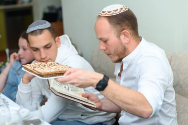 Jewish family celebrate Passover Seder reading the Haggadah. Young jewish bearded man with kippah reads the Passover Haggadah.